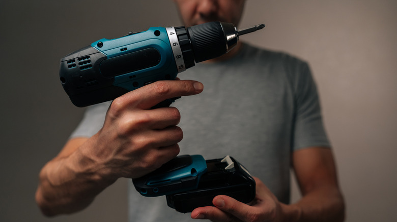 A person in a gray shirt attaching a battery to the bottom of a dark blue/teal battery-powered drill