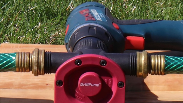 A drill pump on a wooden board outside, attached to a drill