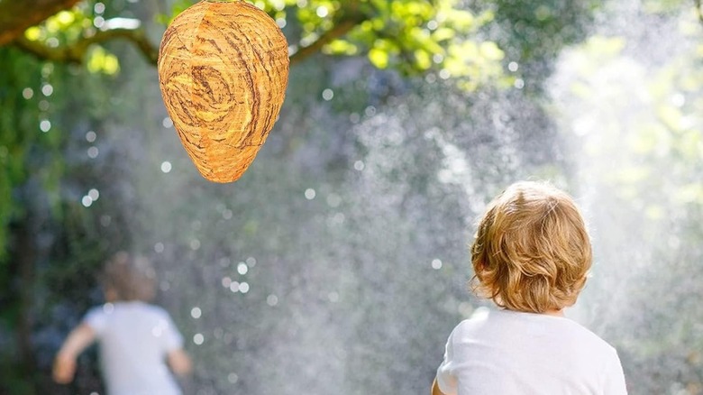 Stingmon fake wasp nest decoy hanging in front of sprinkler in yard with kids playing