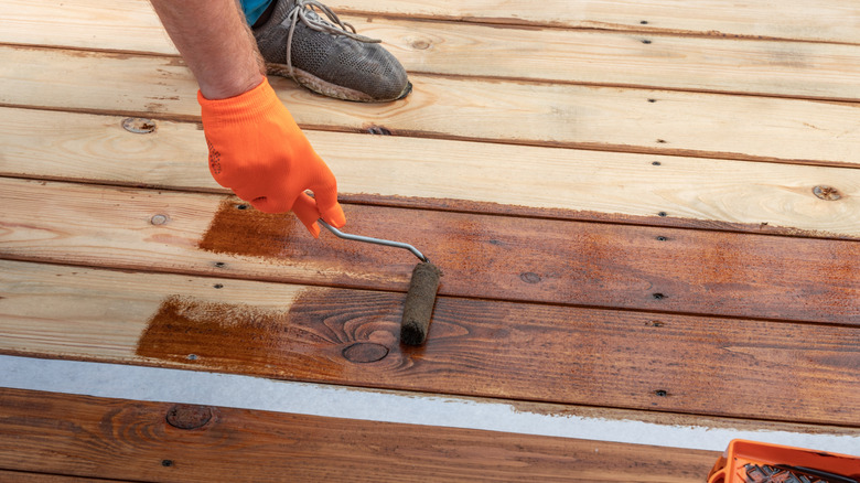 A person using a small roller to apply stain onto a deck