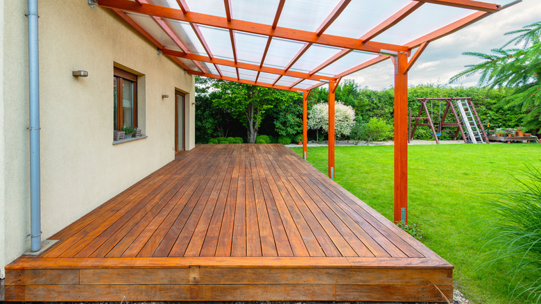 Back deck with dark stained wood, glass overhang, and swing set in background on lawn