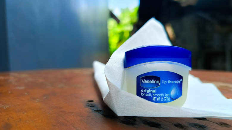 Container of Vaseline sitting on a cloth on top of a worn, wooden table.