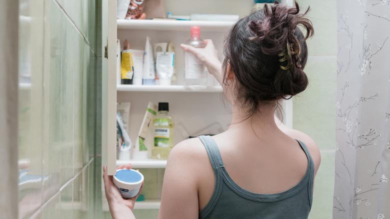 Woman looking at products in a bathroom medicine cabinet.