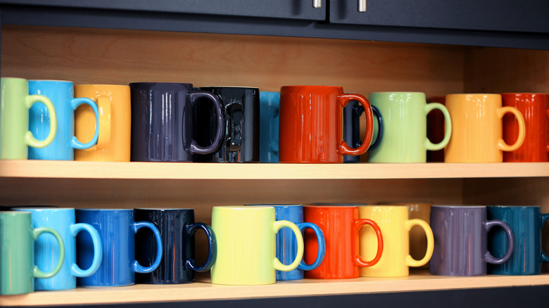 Colorful coffee mugs on shelves in a kitchen.