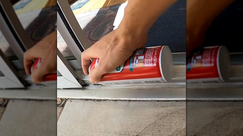 man applying spray lubricant to sliding glass door track