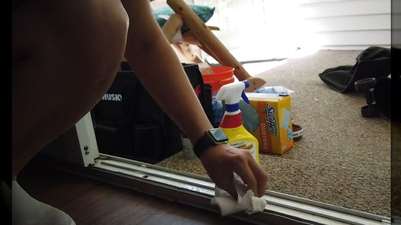 person using paper towel and store bought cleaner to wipe down door tracks