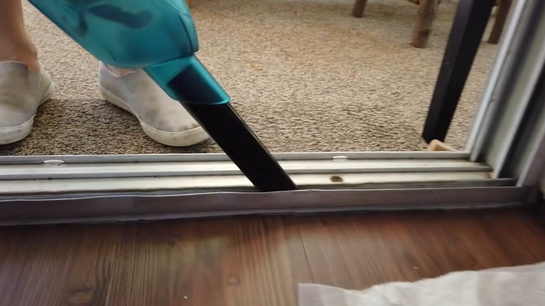 closeup of person using handheld vacuum to clean sliding door frame