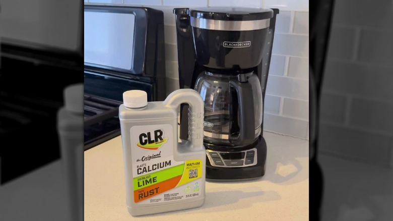 A bottle of CLR Calcium, Lime, and Rust remover on the counter beside a Black + Decker coffee maker.