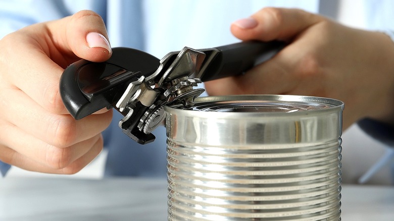 Close-up of a person's hands positioning a can opener on the edge of a tip