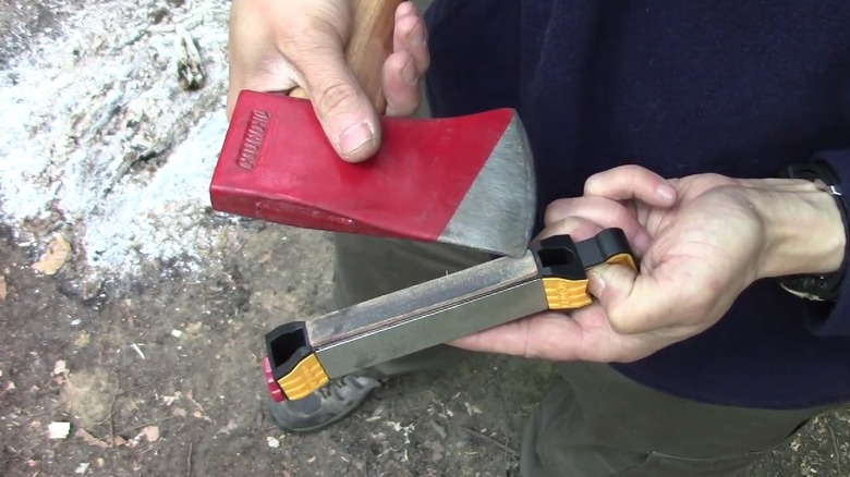 Person using the Work Sharp Guided Field Sharpener on a red axe.