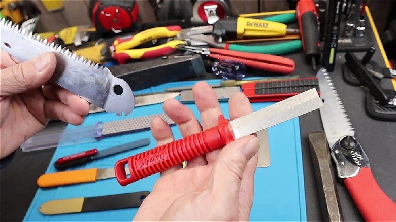 Person's hands holding the Samurai Kanzawa Japanese Saw Diamond Sharpener and a small saw blade among other tools.