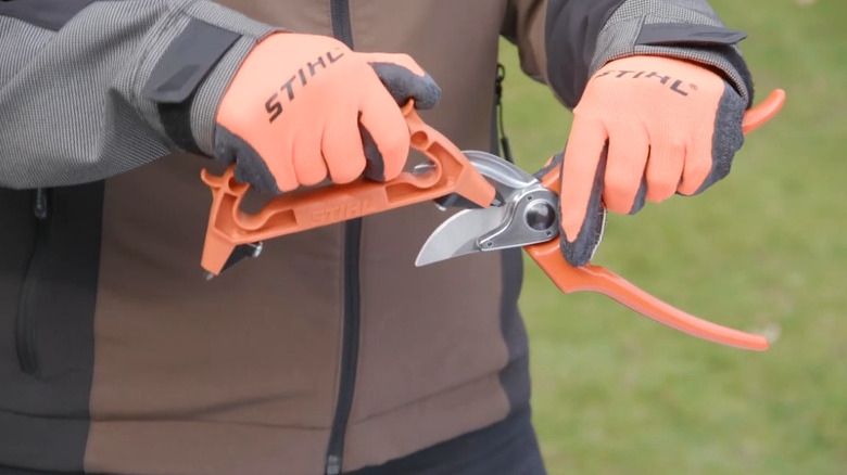 a person wearing orange gloves sharpens hand pruners using the All-In-1 Sharpening Device
