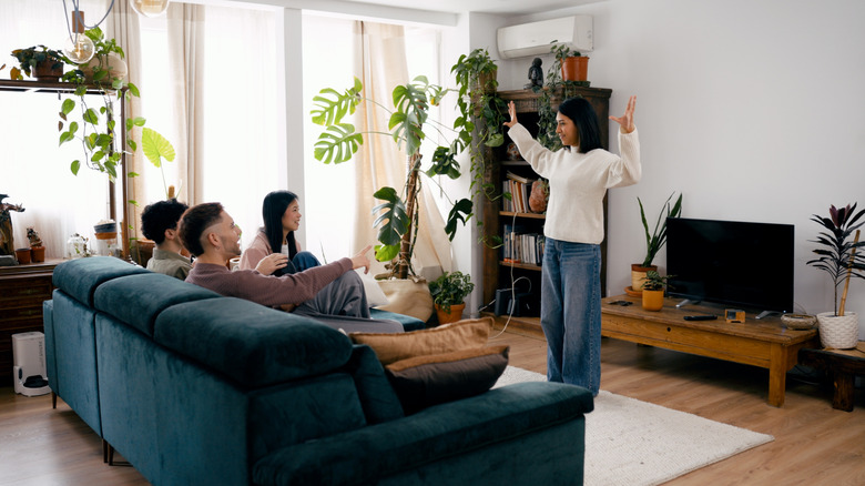 Friends playing charades in a cozy living room filled with plants and books
