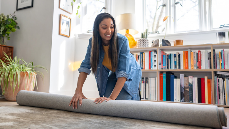 A woman unrolling a rug while decorating in her home