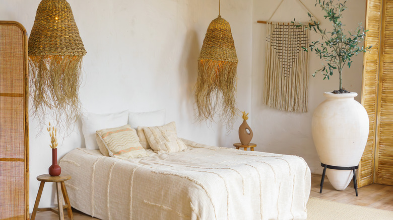 A bedroom with neutral walls and bedding, hanging wicker lamps, and a woven tapestry