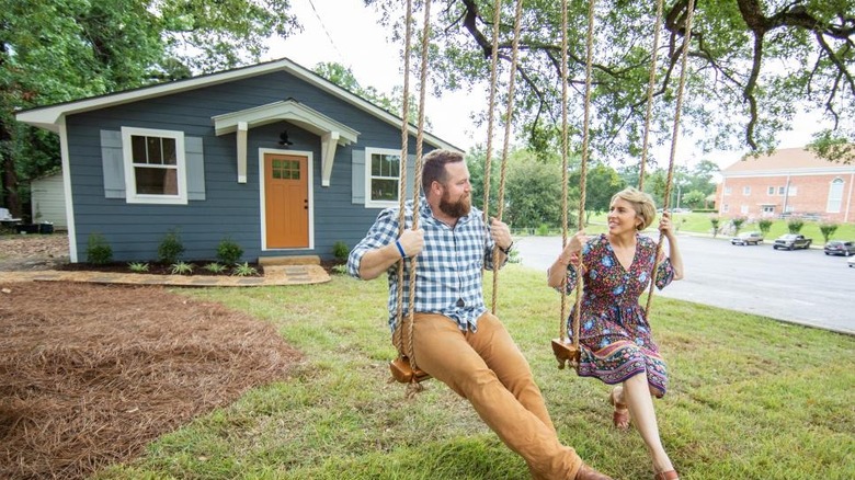 Erin Napier and Ben Napier swinging in front of a small country home