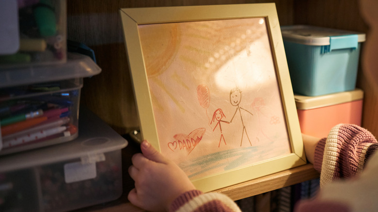 Hands looking at framed children's art of stick figures