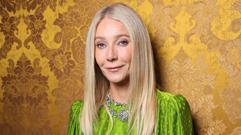 Gwyneth Paltrow smiling in front of a gold brocade wall