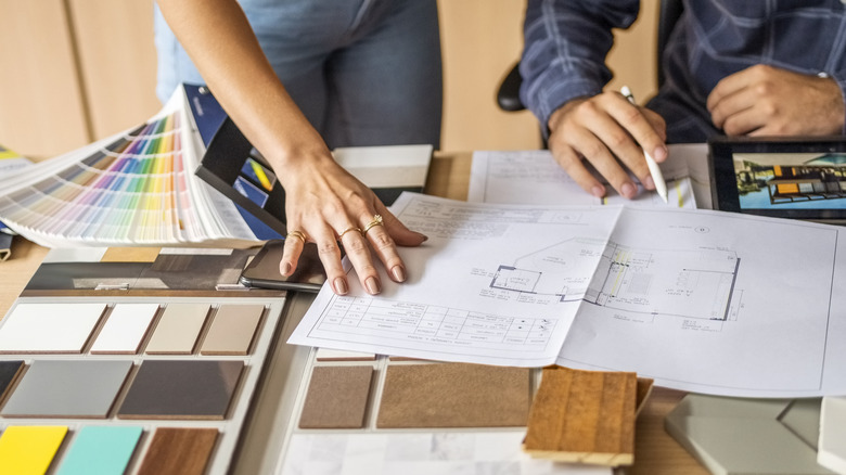 Two people designing a home with blueprints, material samples, and paint samples on a table