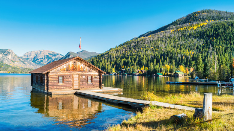 A wood cabin on a lake with beautiful sunny mountains in the back