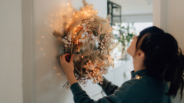 Young woman decorating her house by hanging a wreath on the wall