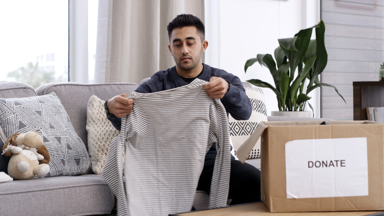 A bearded man folds clothes to go into a donation box.