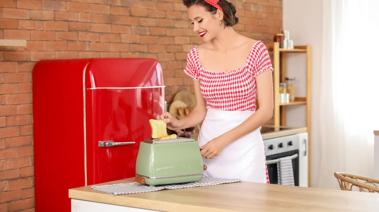 1950s housewife placing bread into a green toaster in the kitchen