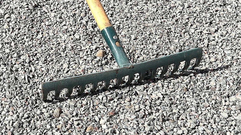 A gravel rake with a green head sits in a pile of leveled gravel