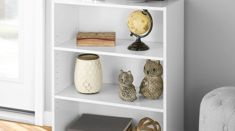 A small white bookshelf is filled with knickknacks