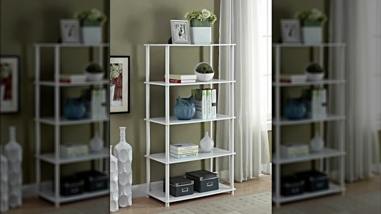 A small white bookshelf laden with books and decor