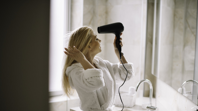 Young woman blow drying hair in bathroom