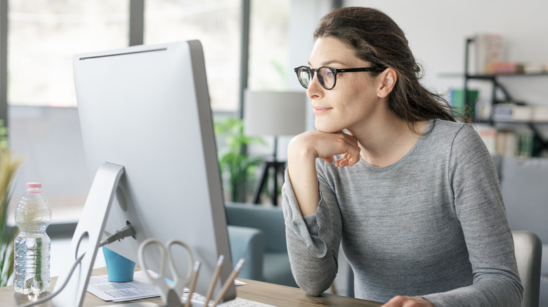 Young woman with glasses browsing desktop computer