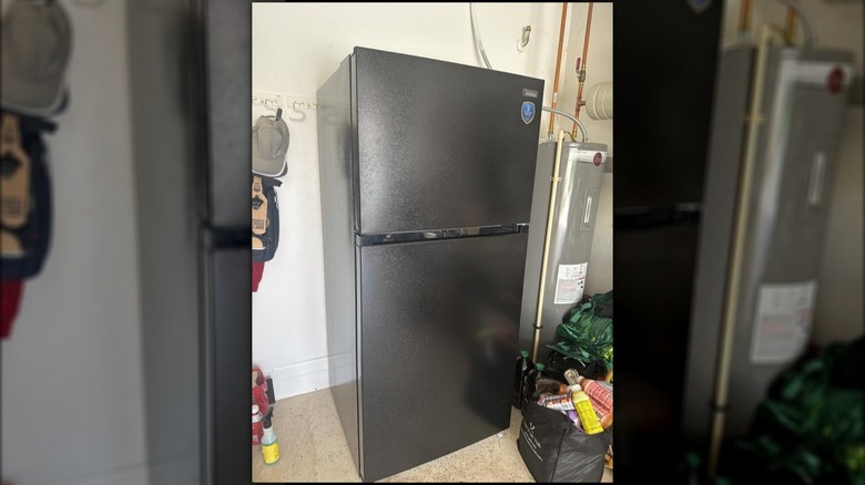 Black Midea fridge stored in the garage alongside clutter