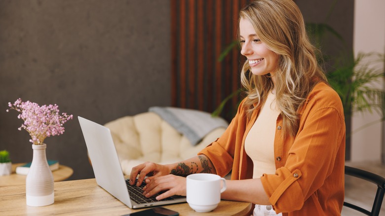 Young woman working on laptop with mug and flower pot