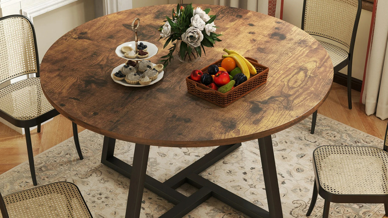 A basket of fruit, flower arrangement, and tea tray it on a rustic wood dining table