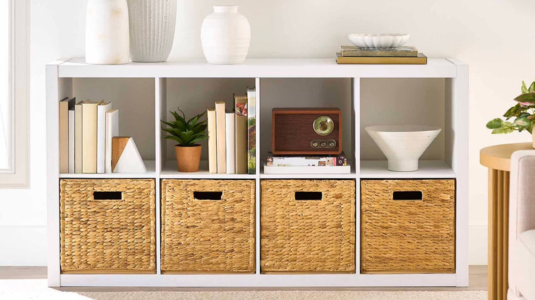 A white 8-cube storage unit is filled with wicker baskets and books