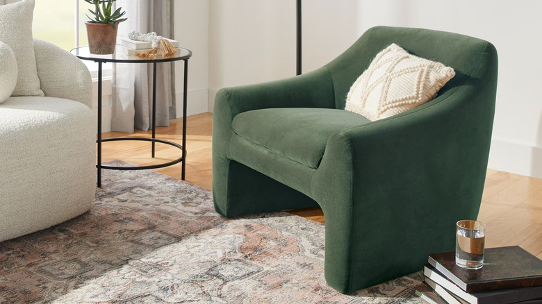 A stack of books and a small coffee table sit next to a green upholstered accent chair