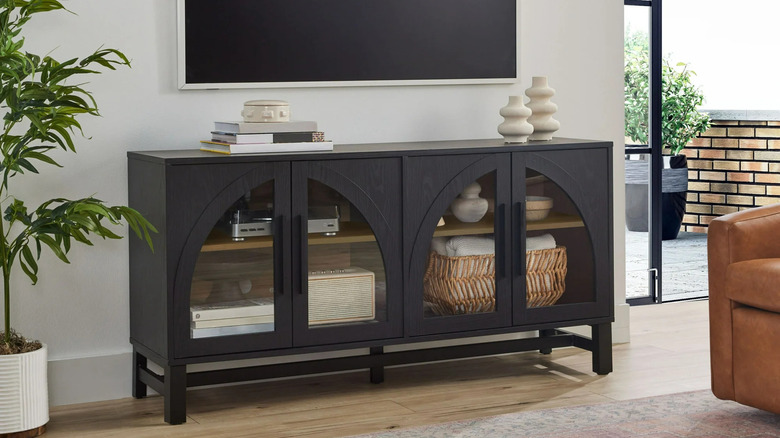 A flat screen tv hangs on the wall above a black arched stand filled with decorative items