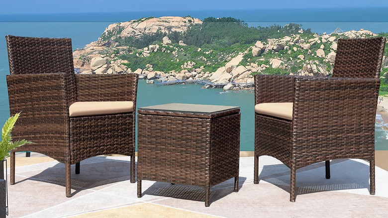 Two wicker chairs and a small table sit on a patio overlooking a bay