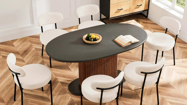 Six white Mid Century Modern upholstered chairs sit around a black and wood dining table