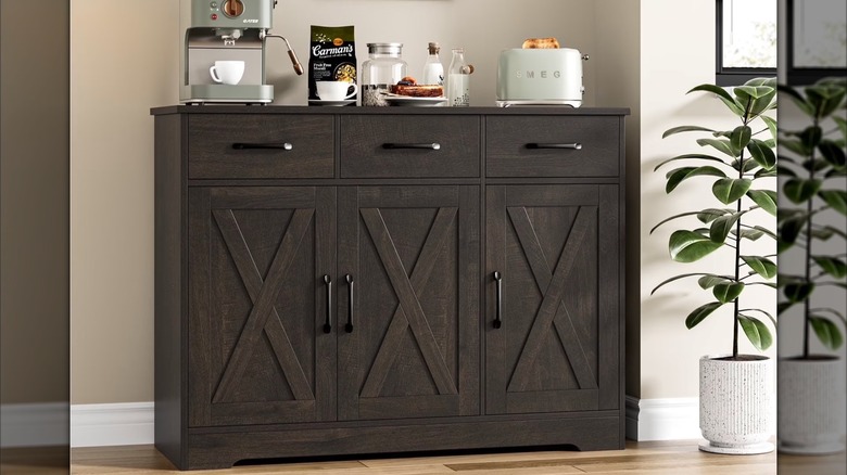 A coffee maker and toaster sit on a dark walnut storage cabinet next to a potted fiddle leaf plant