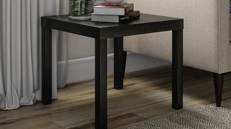 A stack of books sits on a black Parsons end table