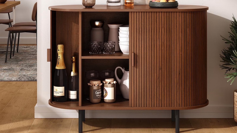 The tambour doors of a Marnur Sideboard Buffet Cabinet are open to reveal stacked dishes and bottles of champagne