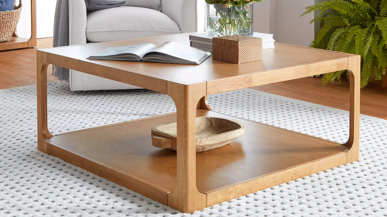 An open book and decorative items sit on a honey-colored wood coffee table