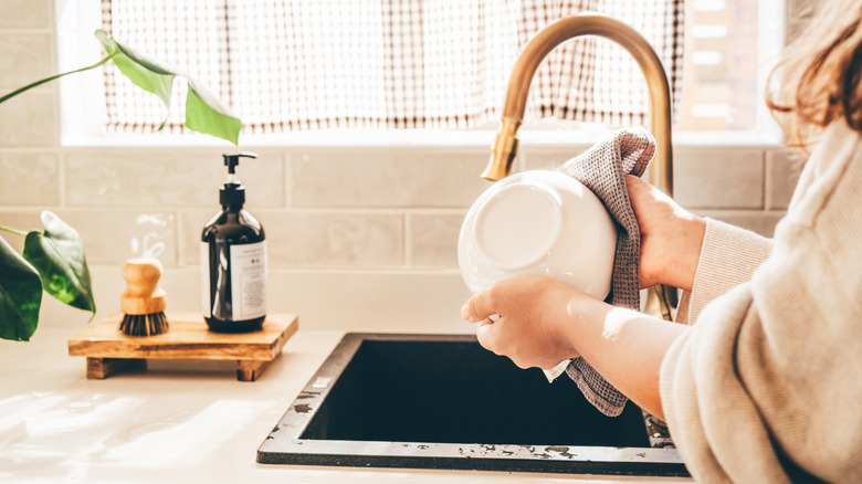 A woman washes a white bowl in a kitchen sink