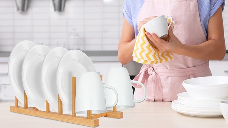 A person uses a yellow dishcloth to dry a mug next to a Sambuteco Bamboo Wooden Dish Drying Rack