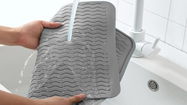 A person rinses off a gray ZLR Silicone Dish Drying Mat