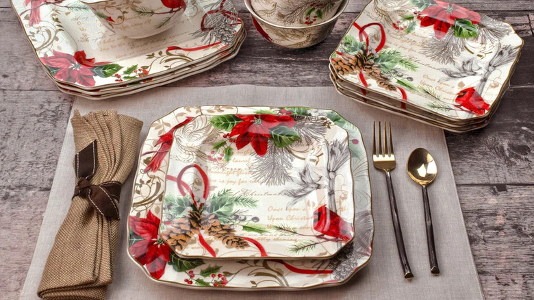 A holiday dinnerware set that looks like traditional wrapping paper, with script-style writing, red cardinals, and poinsettia flowers detailed on the surfaces.