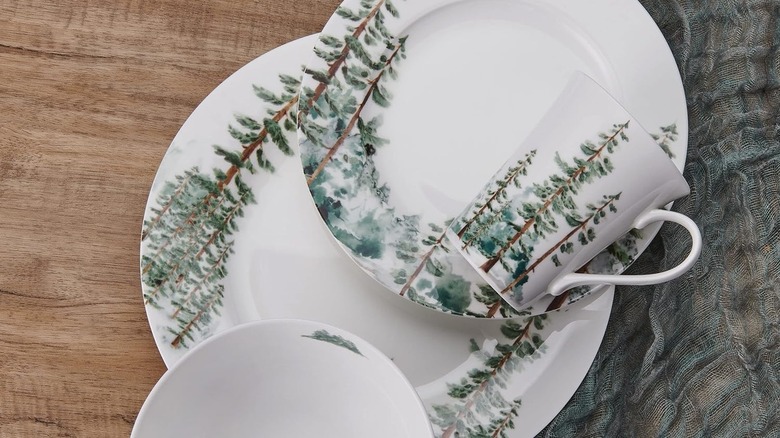 A white dinner set decorated with watercolor evergreen trees.