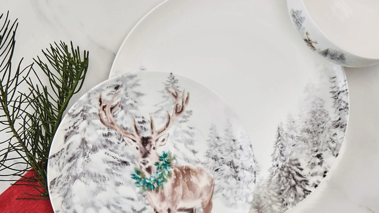 A festive dinner set featuring a deer in front of a wintery forest sits on top of a wooden plank.